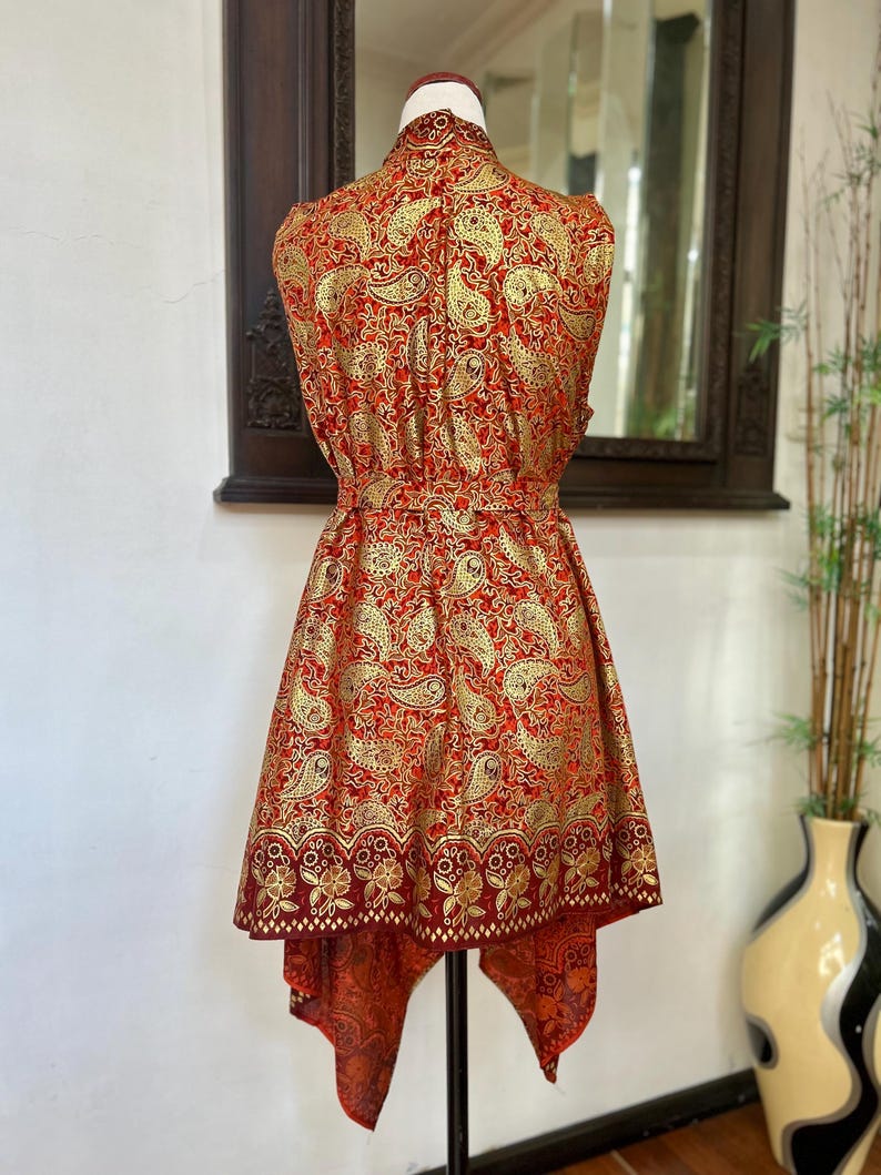 May include: A sleeveless red and gold paisley print dress with a high neckline and a high-low hemline.
