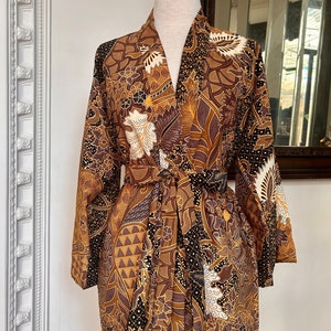 May include: A brown and gold patterned kimono robe with a tie belt. The robe has a floral and geometric design.