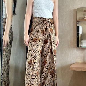 May include: A white one-shoulder top paired with wide-leg pants featuring a brown and gold floral print. The pants have a wrap-around style and a tie at the waist.