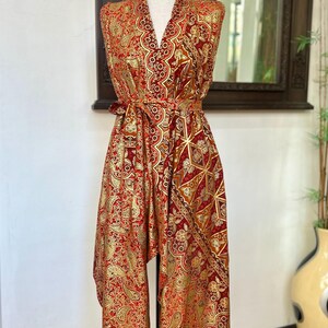 May include: A red and gold patterned sleeveless dress with a V-neckline and a tie at the waist. The dress has a geometric pattern and is made of a silky fabric.