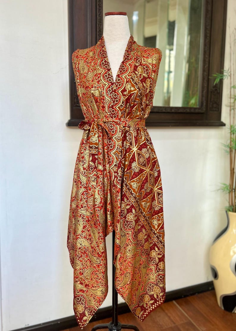 May include: A red and gold patterned sleeveless dress with a V-neckline and a tie at the waist. The dress has a geometric pattern and is made of a silky fabric.