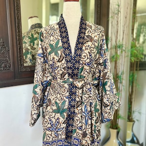 May include: A white, blue, and green patterned kimono with a black and blue trim. The kimono has a sash and is tied at the waist.