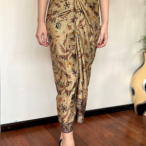 Peut inclure: Une jupe à motif brun et or avec une ceinture marron et une boucle argentée. La jupe est faite d'un tissu doux et fluide et a un design drapé. La jupe est portée par une personne avec des jambes nues et des sandales à talons noirs.