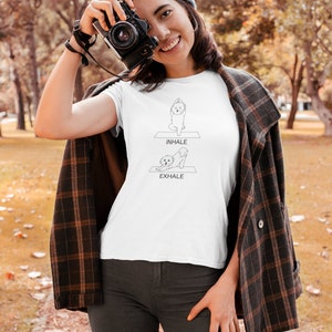 May include: White t-shirt with a black line drawing of a dog doing yoga poses. The text "INHALE" and "EXHALE" are printed on the shirt.