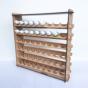 Könnte beinhalten: Ein Holzregal zur Aufbewahrung von Farbflaschen mit mehreren Regalbrettern und Fächern zur Aufnahme kleiner Flaschen. Das Regal ist aus hellem braunem Holz gefertigt und hat ein schlichtes Design.