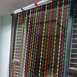 May include: A colorful beaded curtain made of yarn with tassels at the bottom. The curtain is made of multiple strands of yarn, each with a different color. The curtain is hanging in a doorway.