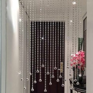 May include: A crystal beaded curtain hangs in a doorway, creating a shimmering, elegant divider. The beads are clear and reflect light, adding a touch of sparkle to the space.