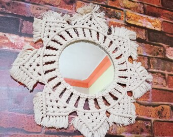 May include: A white macrame mirror with a round mirror in the center. The mirror is hanging on a brick wall.