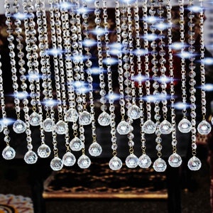 Op de afbeelding: Een gordijn gemaakt van strengen van heldere kristallen kralen met een traanvorm aan de onderkant. De kralen zijn geregen aan een dunne gouden draad.