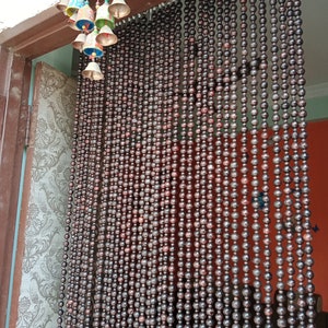 May include: A brown wooden bead curtain hangs in a doorway. The beads are round and have a dark brown colour. The curtain is made of many strands of beads, and it is hanging from a wooden frame.