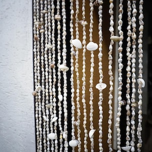 Peut inclure: Un rideau de perles blanches en coquillages. Le rideau est suspendu dans une porte et est composé de plusieurs fils de perles.