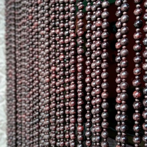 May include: A close-up of a brown wooden beaded curtain. The beads are round and have a smooth, polished finish. The curtain is hanging in a doorway or window.