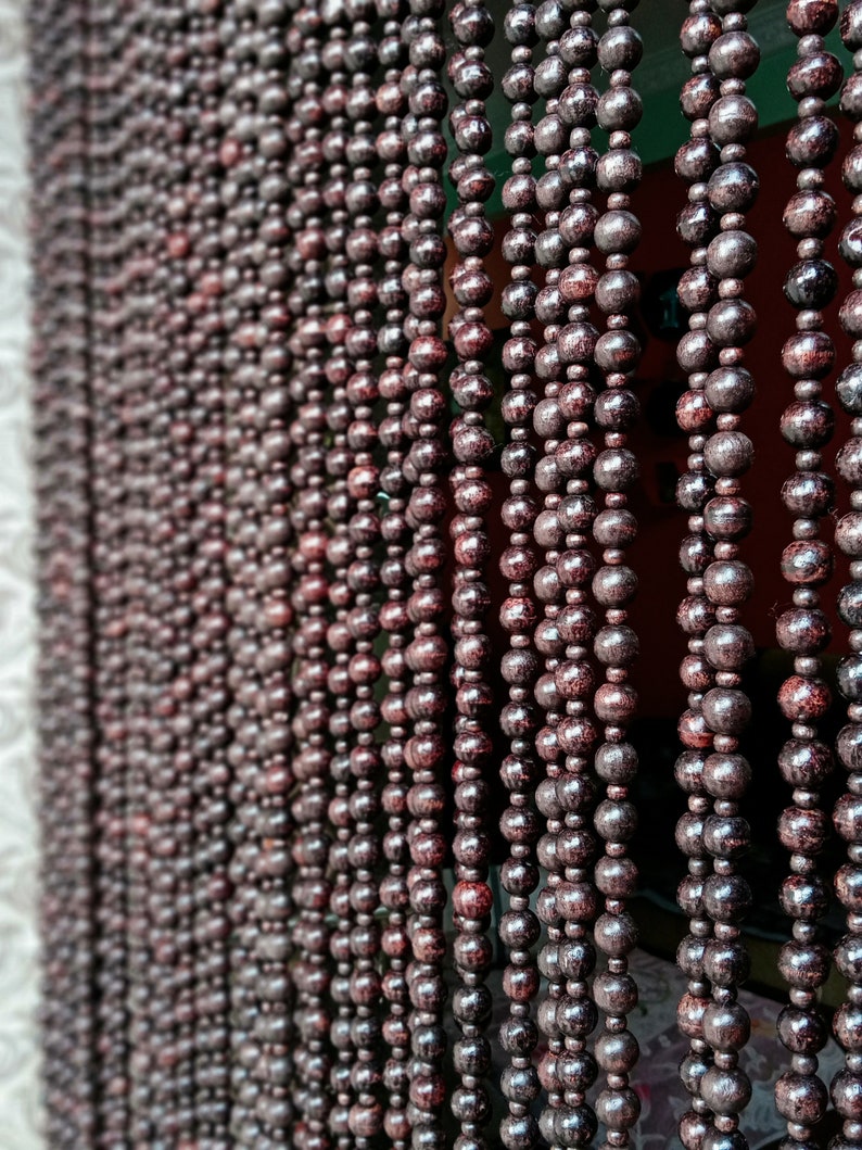 May include: A close-up of a brown wooden beaded curtain. The beads are round and have a smooth, polished finish. The curtain is hanging in a doorway or window.