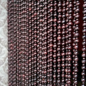 May include: A close-up of a brown beaded curtain. The beads are round and have a smooth, polished finish. The curtain is made of many strands of beads, which are hung from a rod.