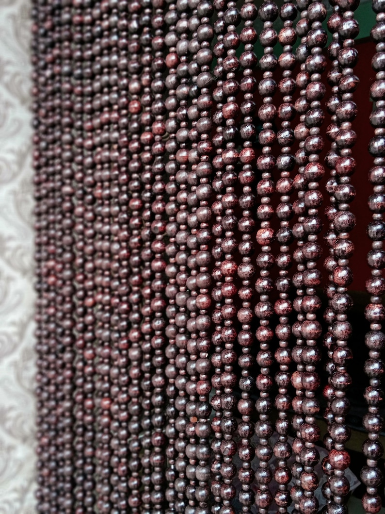 May include: A close-up of a brown beaded curtain. The beads are round and have a smooth, polished finish. The curtain is made of many strands of beads, which are hung from a rod.