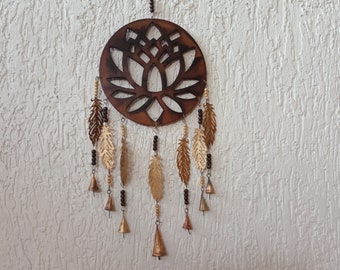 Op de afbeelding: Een bruine houten droomvanger met een lotusbloemdessin en gouden veren die eraan hangen. De droomvanger heeft bruine kralen en kleine belletjes die eraan hangen.