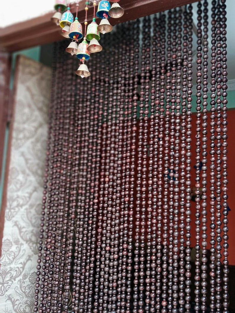 May include: A brown wooden bead curtain hangs in a doorway. The beads are round and have a dark brown colour. The curtain is made of many strands of beads, and it is hanging from a wooden frame.