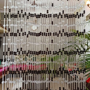 May include: A beaded curtain made of clear and black round beads. The beads are strung on thin wires and hang in rows. The curtain is hanging in a doorway.
