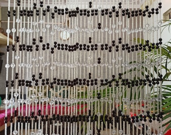 May include: A beaded curtain made of clear and black round beads. The beads are strung on thin wires and hang in rows. The curtain is hanging in a doorway.