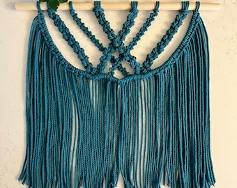 May include: Teal blue macrame wall hanging with a wooden dowel at the top and fringe at the bottom.