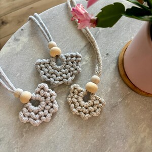 May include: Three macrame wall hangings with wooden beads. Each hanging is in the shape of a flower with a circular opening in the center. The hangings are a light beige color.