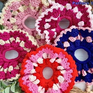 May include: A collection of handmade crochet hair scrunchies in various colors. The scrunchies feature a circular design with open centers and are in shades of pink, red, and blue with white accents. The text "Pattern & tutorial Video" is visible in the image.