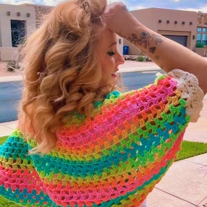 May include: A colorful, open-weave crochet shawl in a rainbow of hues, including pink, orange, yellow, green, and blue. The shawl has a cream-colored border. The text "Pattern & Video Tutorial" is visible in the lower left corner.