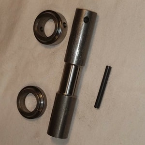 May include: A set of three silver metal parts for a piece of machinery. The parts include a long cylindrical piece with a hole in the center, a smaller cylindrical piece with a hole in the center, and a small metal pin.