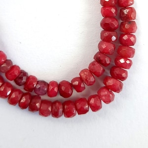 May include: A strand of red gemstone beads. The beads are faceted and have a slightly irregular shape. The beads are strung on a clear thread.