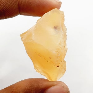 May include: A rough, translucent, orange-colored gemstone with a slightly irregular shape.