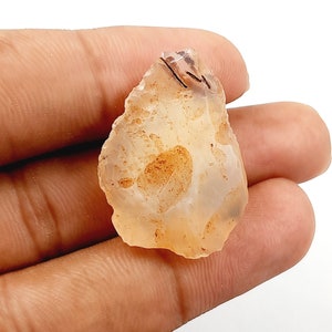 May include: A translucent, light orange agate stone with brown inclusions. The stone is irregularly shaped and has a rough, natural texture.