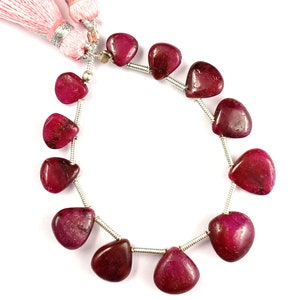 Peut inclure: Un collier de pierres précieuses polies, en forme de cœur, de couleur rouge foncé. Les perles sont enfilées sur un fil d'argent, avec un pompon rose en haut. Les pierres ont une finition lisse et brillante. Idéal pour la création de bijoux.