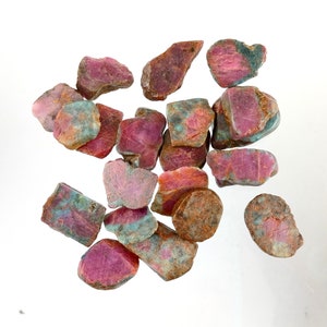 May include: A collection of pink and green ruby rough stones. The stones are various shapes and sizes.