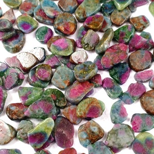 Puede incluir: Una colección de pequeñas piedras preciosas multicolores de forma irregular. Las piedras son una mezcla de verde, rosa, rojo y azul.