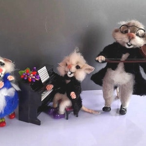 Può includere: Tre figurine di topo in feltro che suonano musica. Un topo indossa un vestito blu e un fiocco blu, un altro suona il pianoforte e il terzo suona il violino.