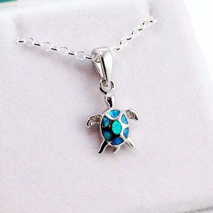 May include: A silver necklace with a blue opal turtle pendant. The necklace is in a white box with a turquoise lid.
