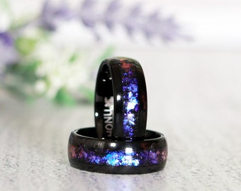 May include: Two black tungsten carbide rings with a galaxy-inspired design. The rings feature a purple, blue, and white nebula pattern. The rings are stacked on top of each other. The text "Orion Nebula" is printed below the rings.