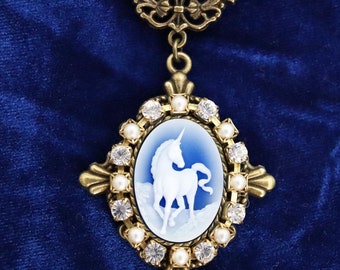 May include: A bronze-toned pendant necklace featuring an oval cameo with a white unicorn relief on a light blue background. The cameo is framed by alternating clear rhinestones and small white pearls, suspended from a decorative bronze chain.