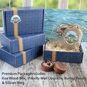 May include: A blue and gold patterned box with a smaller wooden box inside. The wooden box contains a ring. The larger box has a logo that says "The Honu Shirt Company".