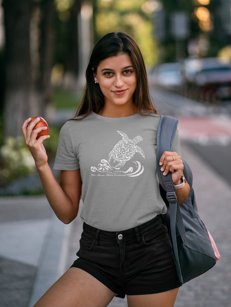 Puede incluir: Una camiseta gris con un gr&aacute;fico blanco de una tortuga hecha de c&iacute;rculos m&aacute;s peque&ntilde;os y olas. El texto "The Aloha Shirt Company" est&aacute; impreso debajo de la tortuga.