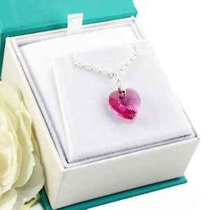 Op de afbeelding: Een zilveren ketting met een roze kristallen hart hanger in een witte geschenkdoos.