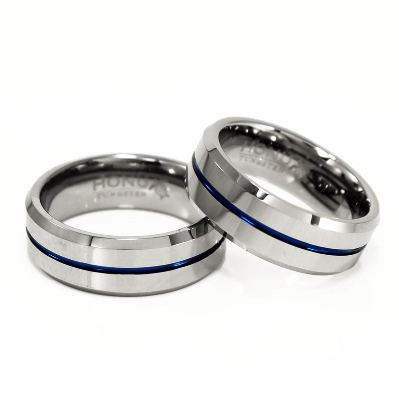 K&ouml;nnte beinhalten: Zwei silberne Ringe aus Wolframcarbid mit einer blauen Linien-Einlage. Die Ringe sind abgeschr&auml;gt und haben das Wort "HONOR" auf der Innenseite eingraviert.
