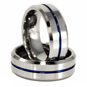 K&ouml;nnte beinhalten: Zwei silberne Wolframcarbidringe mit einer blauen Einlage. Die Ringe sind abgeschr&auml;gt und haben eine polierte Oberfl&auml;che.