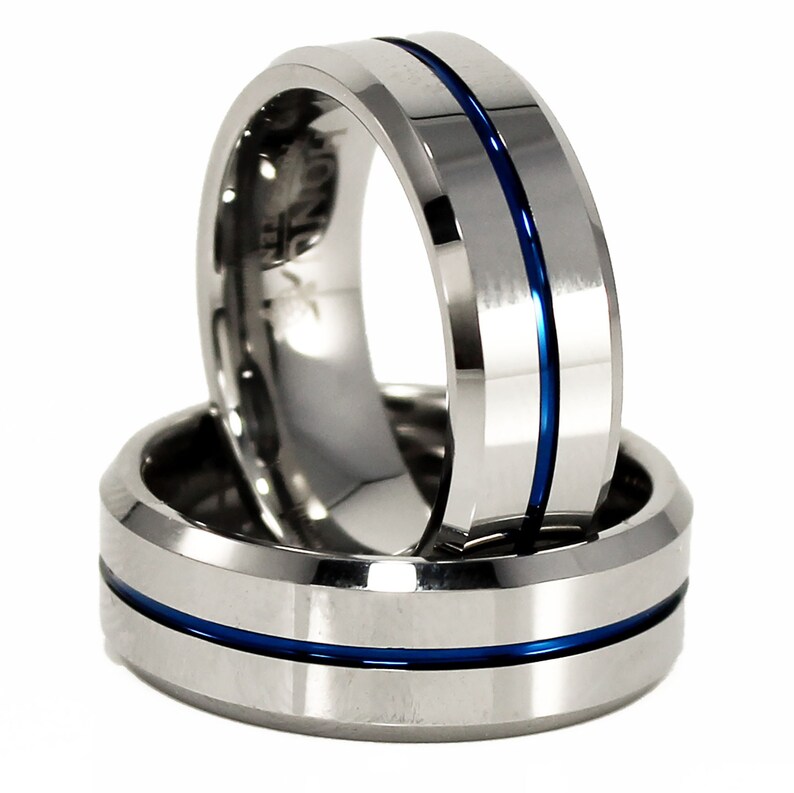K&ouml;nnte beinhalten: Zwei silberne Wolframcarbidringe mit einer blauen Einlage. Die Ringe sind abgeschr&auml;gt und haben eine polierte Oberfl&auml;che.