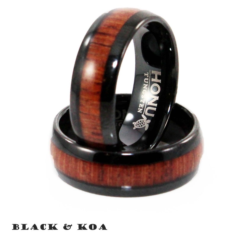 May include: Two black tungsten rings with Koa wood inlay. The rings are stacked on top of each other. The top ring has the word "HONU" and "TUNGSTEN" engraved on the side.