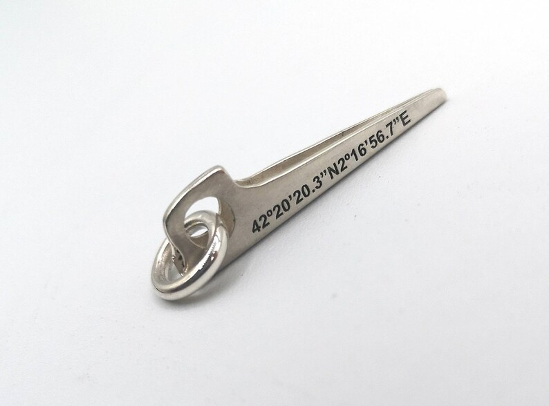 K&ouml;nnte beinhalten: Silberner Schl&uuml;sselanh&auml;nger in Form eines Kletterhammers mit einem Ring. Der Hammer hat die Koordinaten "42&deg;20'20.3"N2&deg;16'56.7"E" eingraviert.