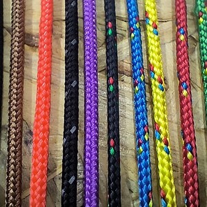 K&ouml;nnte beinhalten: Sortiment an bunten geflochtenen Seilen mit verschiedenen Mustern. Die Seile sind in einer Reihe angeordnet und alle gleich lang.