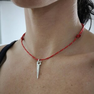 K&ouml;nnte beinhalten: Eine rote Schnurkette mit einem silbernen Anh&auml;nger in Form eines Kletterhammers. Der Hammer tr&auml;gt die Inschrift "Keep It Simple".