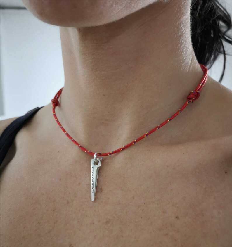 K&ouml;nnte beinhalten: Eine rote Schnurkette mit einem silbernen Anh&auml;nger in Form eines Kletterhammers. Der Hammer tr&auml;gt die Inschrift "Keep It Simple".