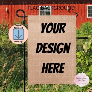 Może przedstawiać: Brązowa flaga ogrodowa z juty z napisem "YOUR DESIGN HERE" w kolorze czarnym. Flaga jest zawieszona na czarnym metalowym drążku przed czerwonym stodołą i zieloną trawą.